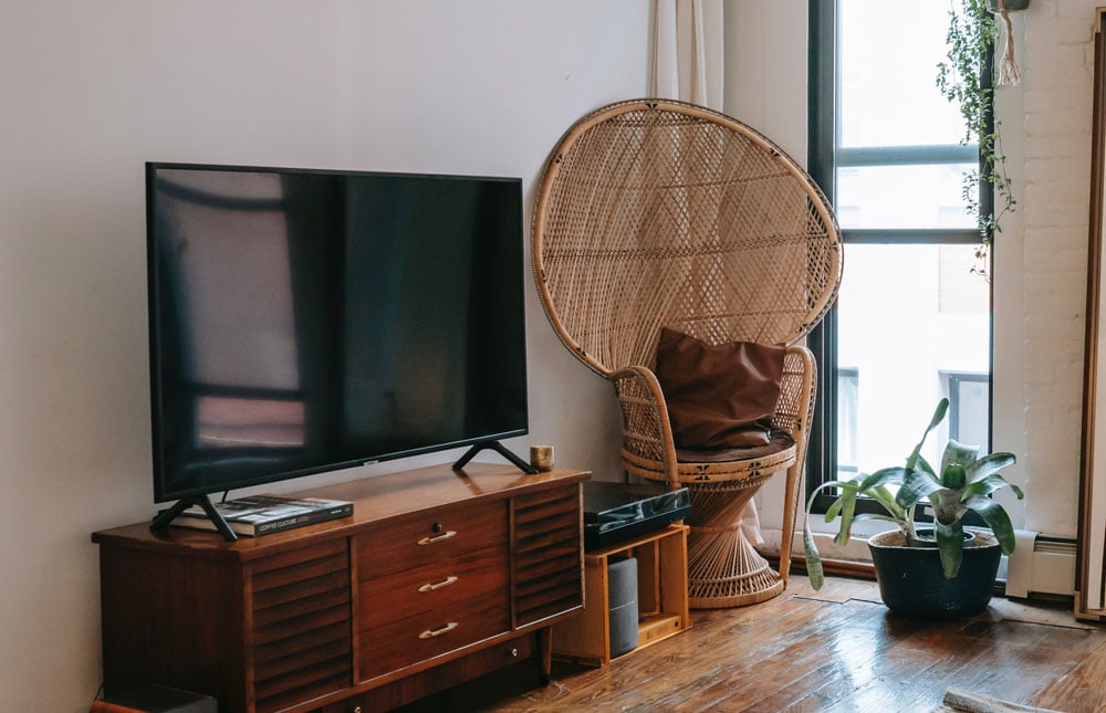 TV on wooden cabinet with wicker chair to right